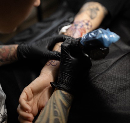 Photo of a tattoo artist finishing a tattoo on a clients forearm.