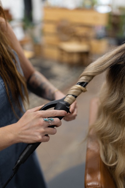 Photo of a stylist curling a blonde clients hair with a curling wand.